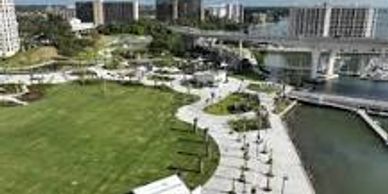 A park with green lawn and pathway near water and buildings.