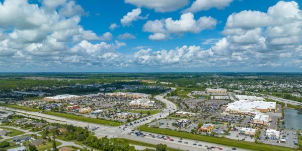 Aerial view of a suburban commercial area with buildings and a highway under a partly cloudy sky.