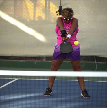 Woman in pink and purple playing pickleball, hitting a yellow ball with a paddle.