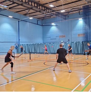 Four adults playing pickleball indoors on a polished wooden court.
