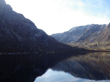 Mountain landscape reflected in calm lake water under a bright sky.