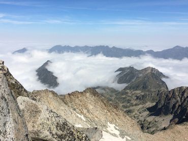 Mountain peaks rising above a sea of clouds under a clear blue sky.