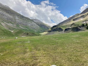 Vast green valley surrounded by mountains under a partly cloudy sky.