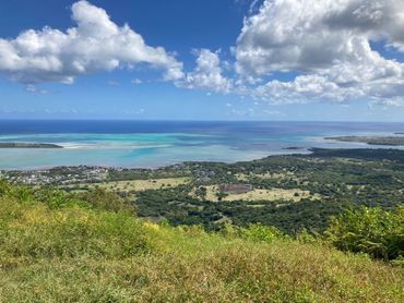Scenic coastal view with lush greenery and turquoise waters under a cloudy blue sky.