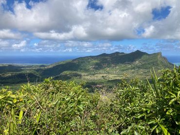 Lush green mountains under a partly cloudy sky with the ocean in the background.