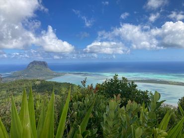 Lush greenery overlooking a mountain and turquoise ocean under a partly cloudy sky.