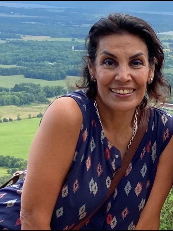 Woman smiling outdoors with scenic countryside in the background.