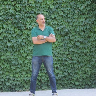 Man standing with crossed arms against a leafy green wall.