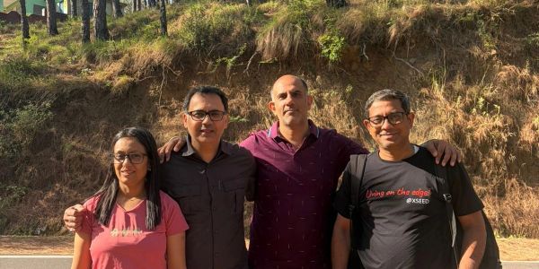 Four people posing outdoors with arms around each other.