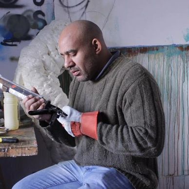 Man intently working on a sculpture while wearing protective gloves.