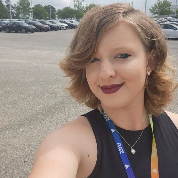 Young woman with styled hair and bold lipstick taking a selfie outdoors in a parking lot.