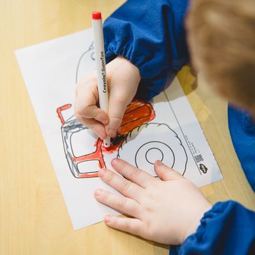 Child coloring a tractor drawing with red marker on paper.