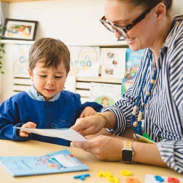 Teacher helping young boy with reading in a classroom.