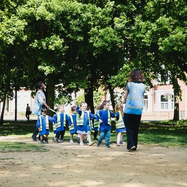 Children in safety vests walking outdoors with teachers.
