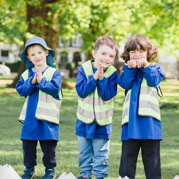 Three young boys in blue shirts and reflective vests posing playfully outdoors.