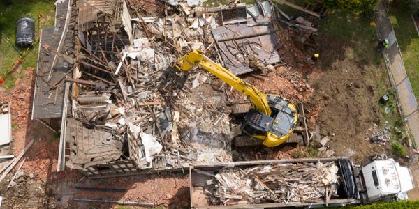 Yellow excavator demolishing a building amid rubble and debris.