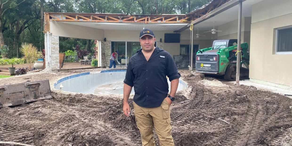 Man standing in front of a house under construction with a pool being built.