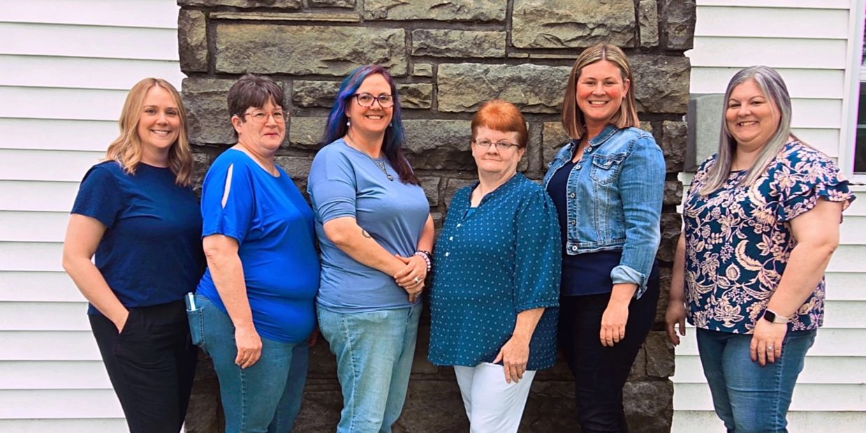 Six women standing together smiling against a stone wall and siding background in Dixon, Missouri