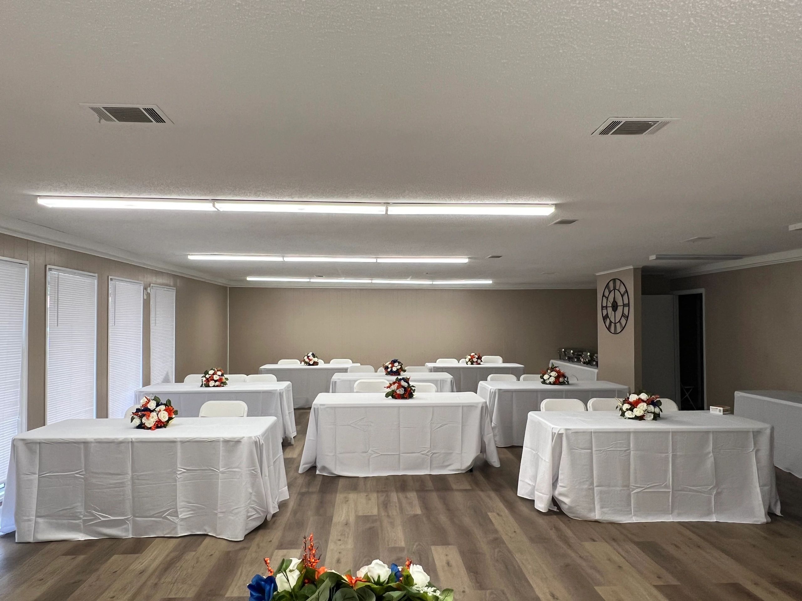 Lou’s Helping Hands event space with rectangular tables, white linens, and floral centerpieces.