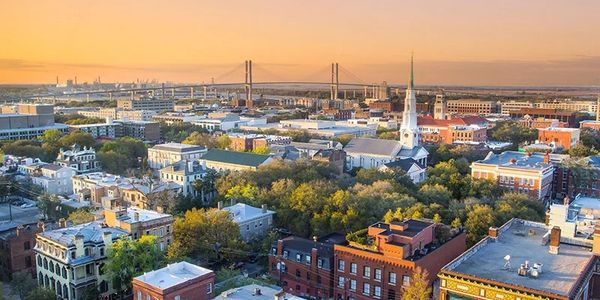 A scenic cityscape at sunset with a prominent bridge and church steeple.