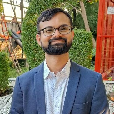 Man with glasses and beard smiling in a suit jacket.