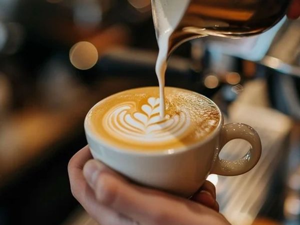 Barista pouring milk to create latte art in a coffee cup.