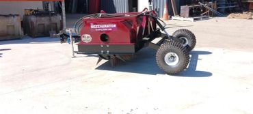 A red wheeled machine labeled BEZZAERATOR on a sunny concrete surface.