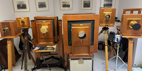 A collection of vintage large format wooden cameras on tripods in a room.