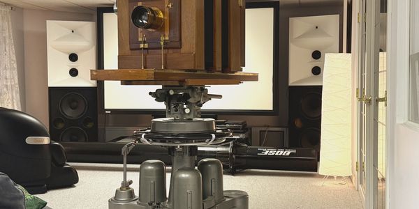 Vintage large-format camera on a tripod in a modern room with speakers and a lamp.