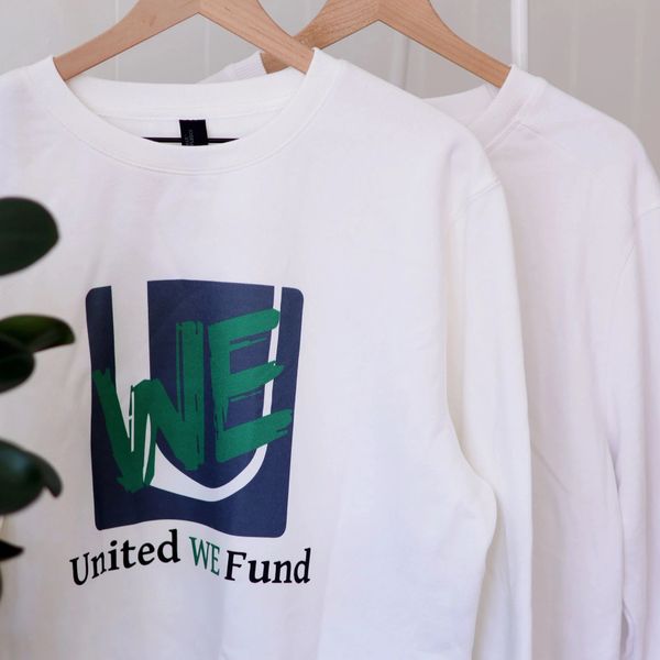 White sweatshirt with United WE Fund logo hanging on wooden hangers.
