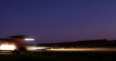 Combine tractor harvesting corn at dusk in Iowa field - Photography by S&C Design Studios