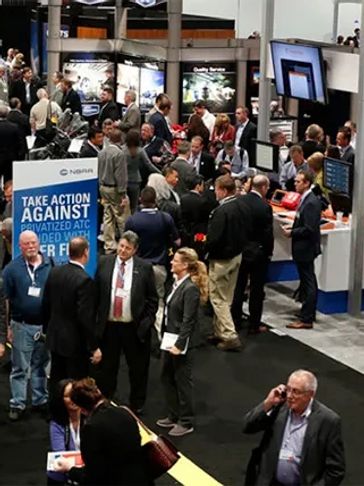 A busy exhibition hall with professionals networking and discussing at booths.