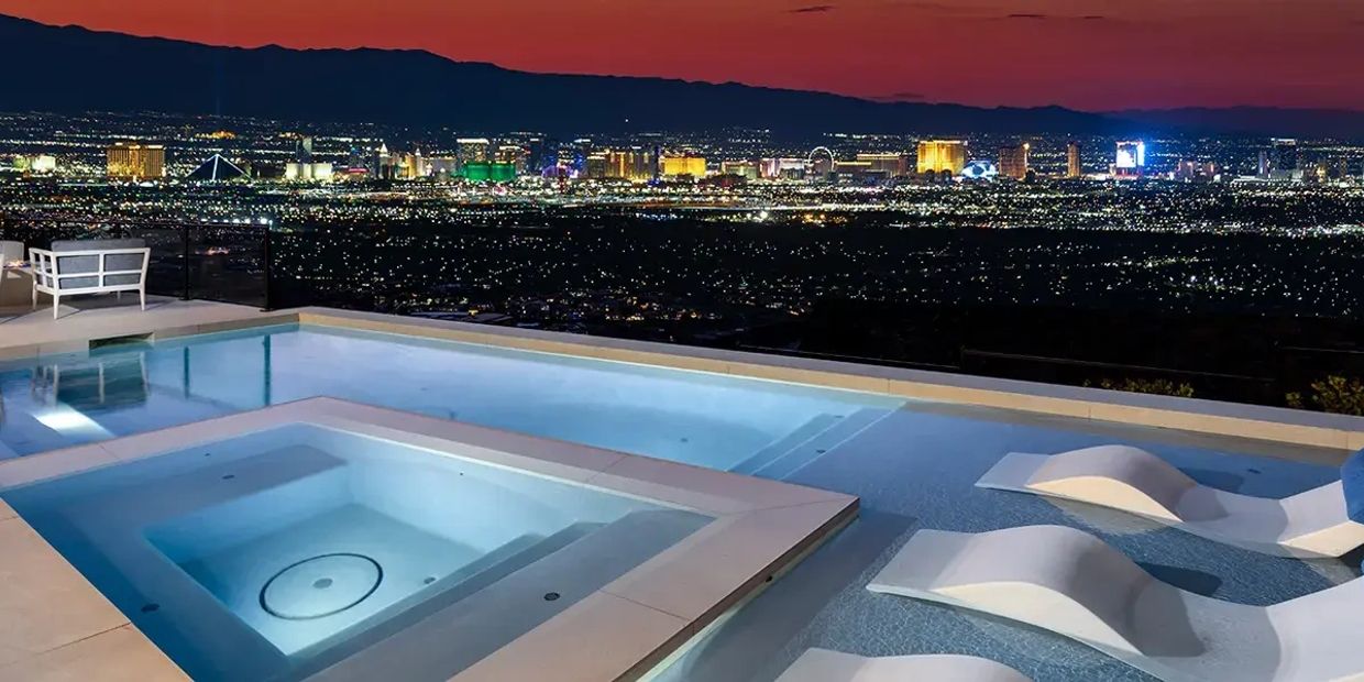 Luxurious pool and hot tub overlooking a brightly lit city skyline at sunset.