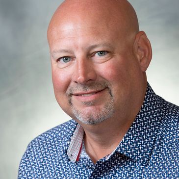 Smiling bald man with blue eyes in patterned shirt.