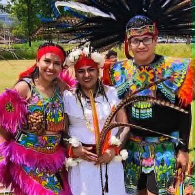 Three people in colorful traditional Aztec dance costumes posing outdoors.