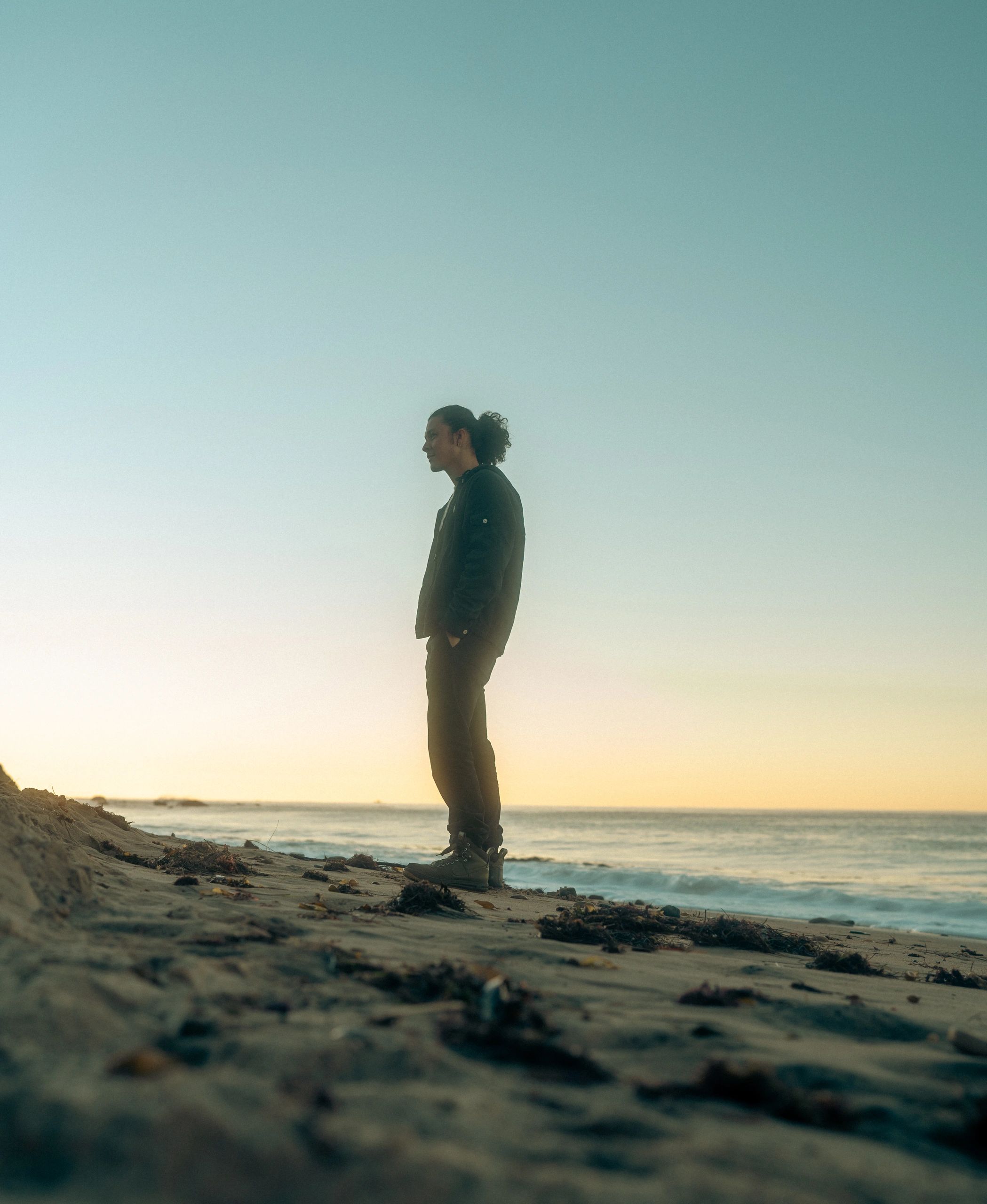 Sunrise photo of man standing on beach waves behind him