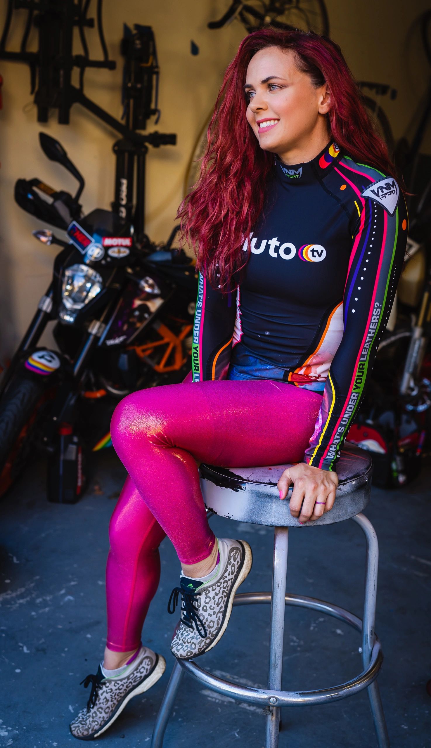 Female model sitting on work stool in her garage working on motorcycle