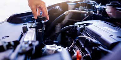 Hand opening a car radiator cap under the hood of a car.