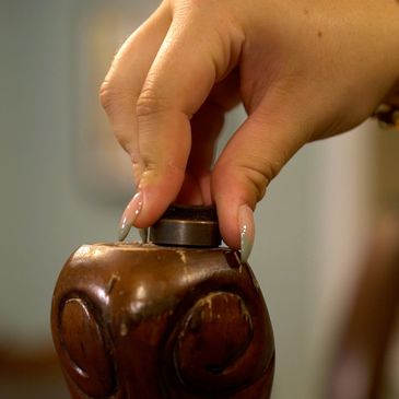 Hand pressing a button on a carved wooden object.