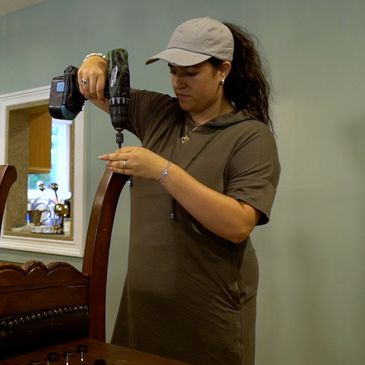 Woman using a drill to fix a chair indoors.