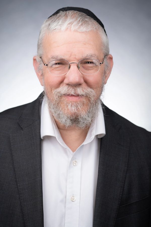 Smiling elderly man with glasses and beard, wearing a suit and kippah.