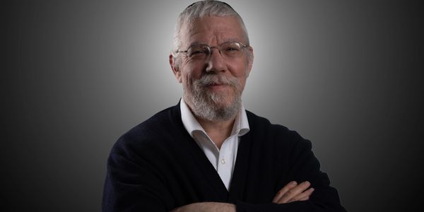 Confident elderly man with glasses and beard, arms crossed, smiling.