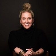Smiling woman in a black turtleneck with hair in a bun against a dark background.