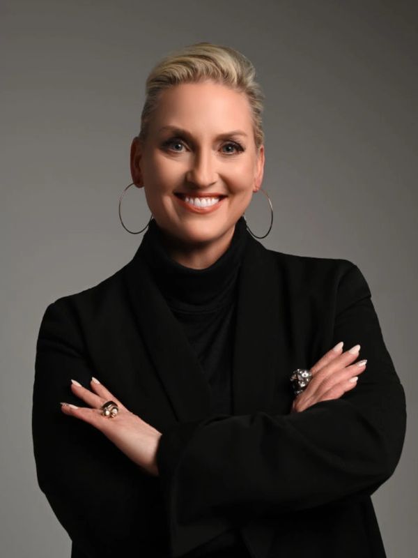 Confident woman in black attire smiling with arms crossed.