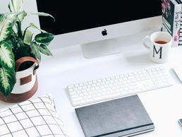 Minimalist workspace with iMac, keyboard, notebook, plant, and coffee mug.