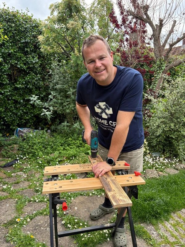 Man using a drill on wood outdoors in a garden.
