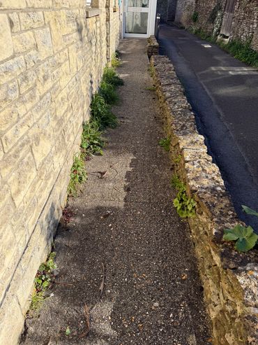 Narrow stone pathway between a brick wall and a low stone fence with some greenery.