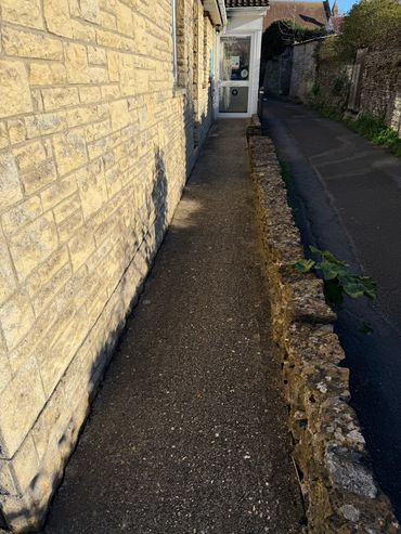 Narrow sidewalk between a stone wall and a small stone barrier alongside a quiet street.