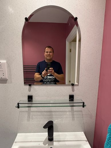 Man taking a selfie in a bathroom mirror with pink walls.