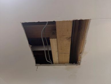 Ceiling with a rectangular hole exposing wooden beams and wires.